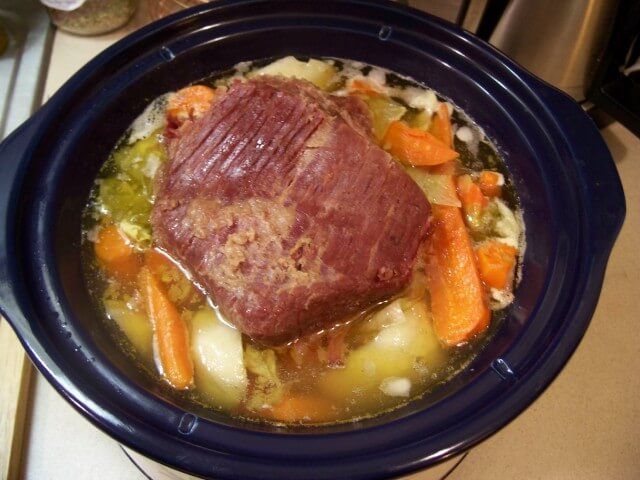 a pot roast with carrots, potatoes and broccoli in a blue bowl