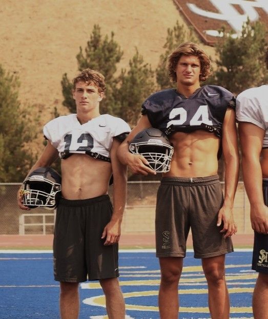 three football players standing on the sidelines with their helmets in front of them, posing for a photo