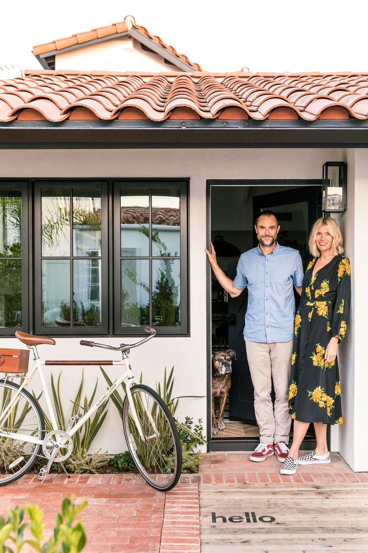 a man and woman standing in front of a house with a bicycle parked outside the door