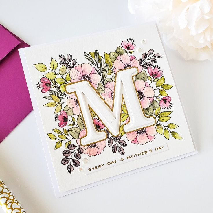 a card with the letter m on it next to some flowers and a pink envelope