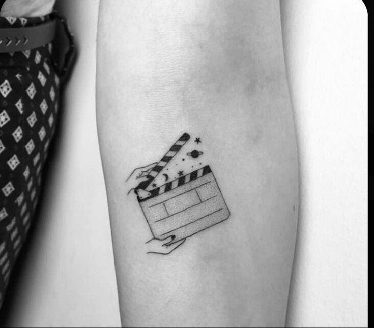 a black and white photo of a movie clapper tattoo on the left inner arm