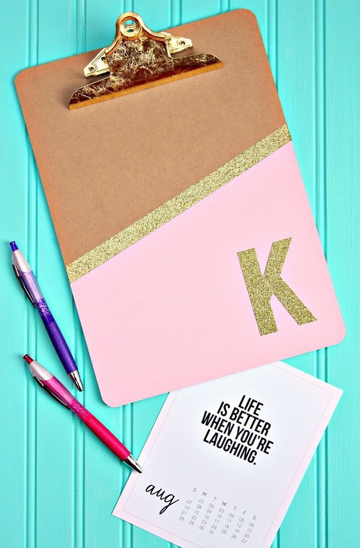 a clipboard with the letter k on it next to two pens and a notepad