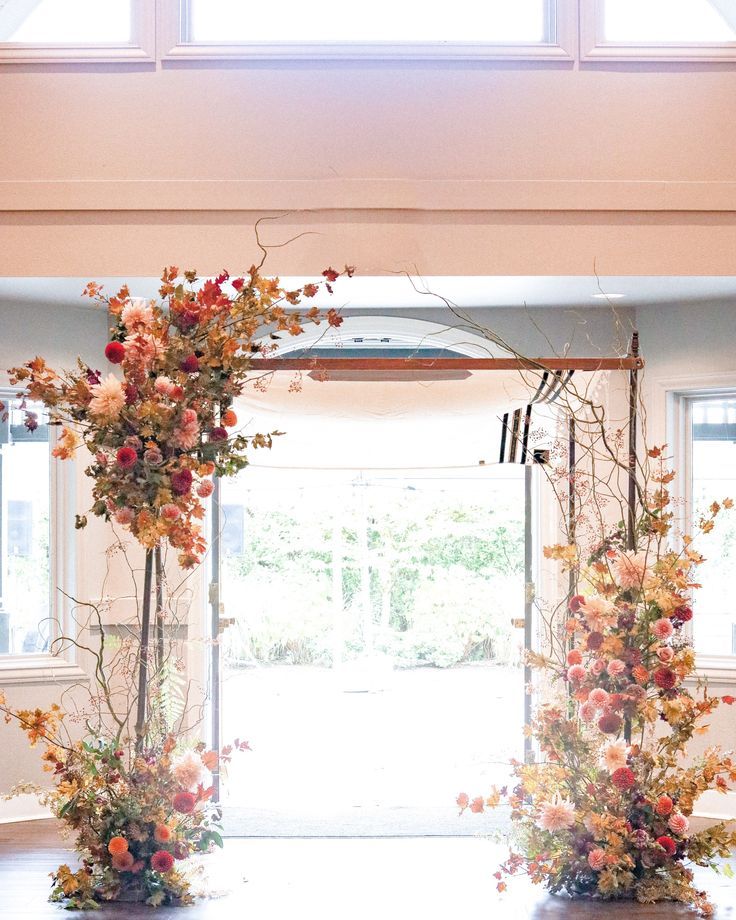 an arch decorated with flowers and branches in front of a door that leads to a patio