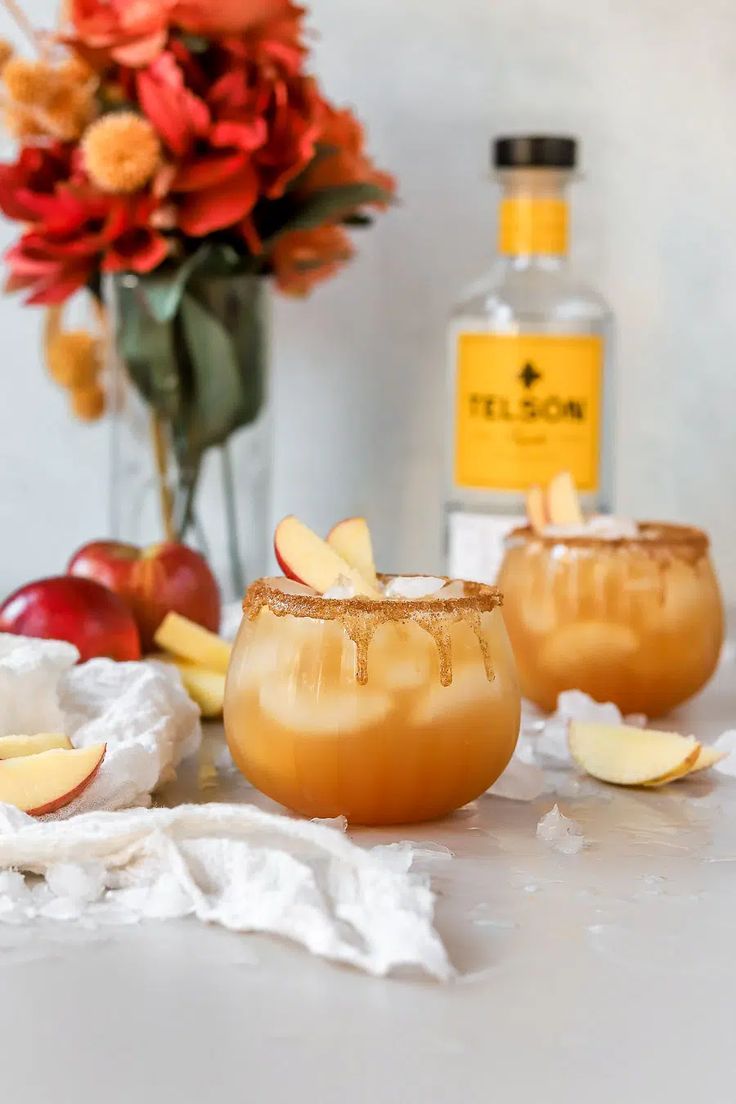 two glasses filled with apple cider on top of a table next to an orange flower