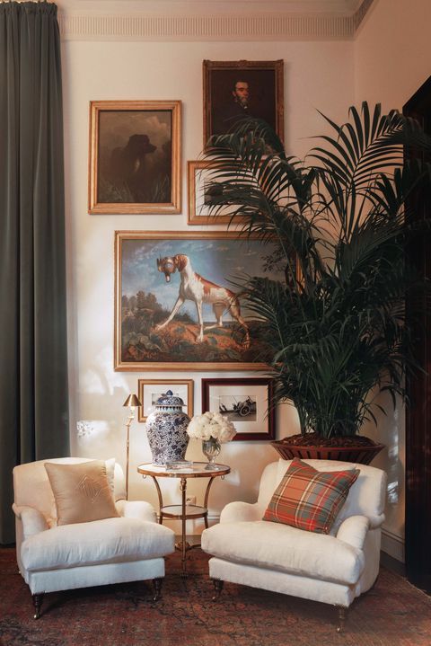 a living room with two white chairs and paintings on the wall above them, along with a vase filled with flowers