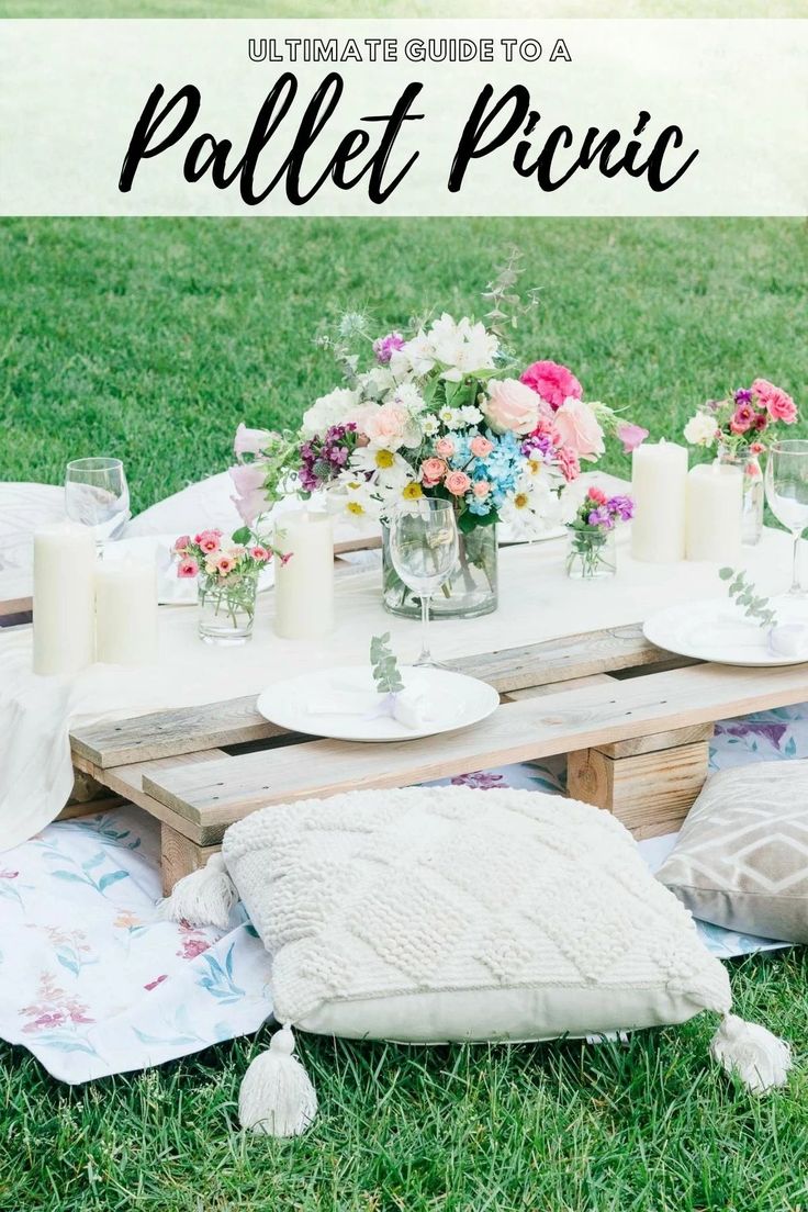 an outdoor table with flowers and candles on it in the grass, surrounded by blankets