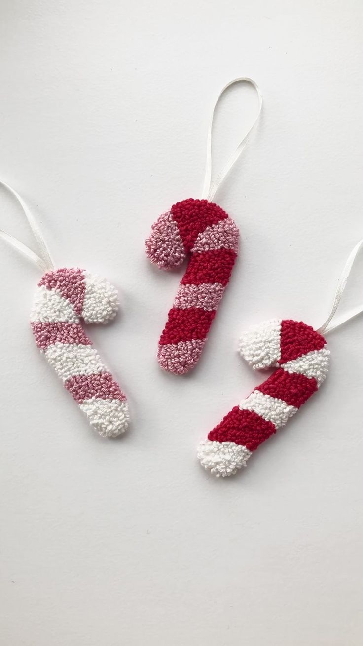 three red and white knitted candy canes ornament hanging from strings on a white surface