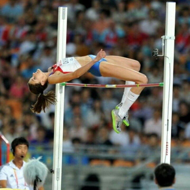 a woman jumping over a high jump in a stadium