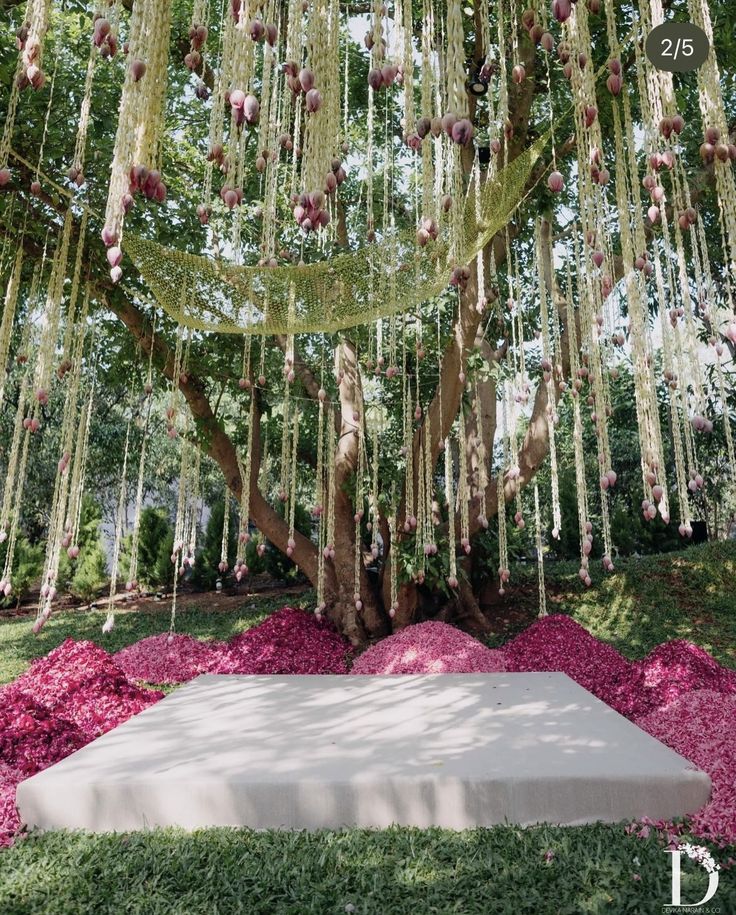 an outdoor ceremony setup with pink flowers and greenery hanging from the ceiling, surrounded by lush green trees