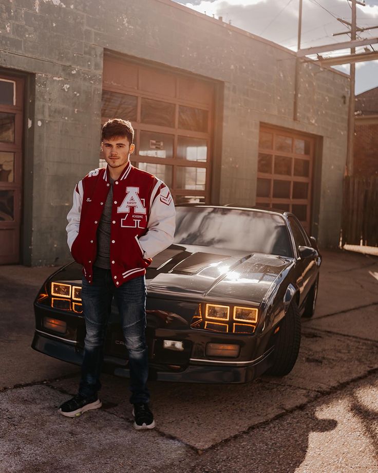 a young man standing next to a car in front of a building with garage doors