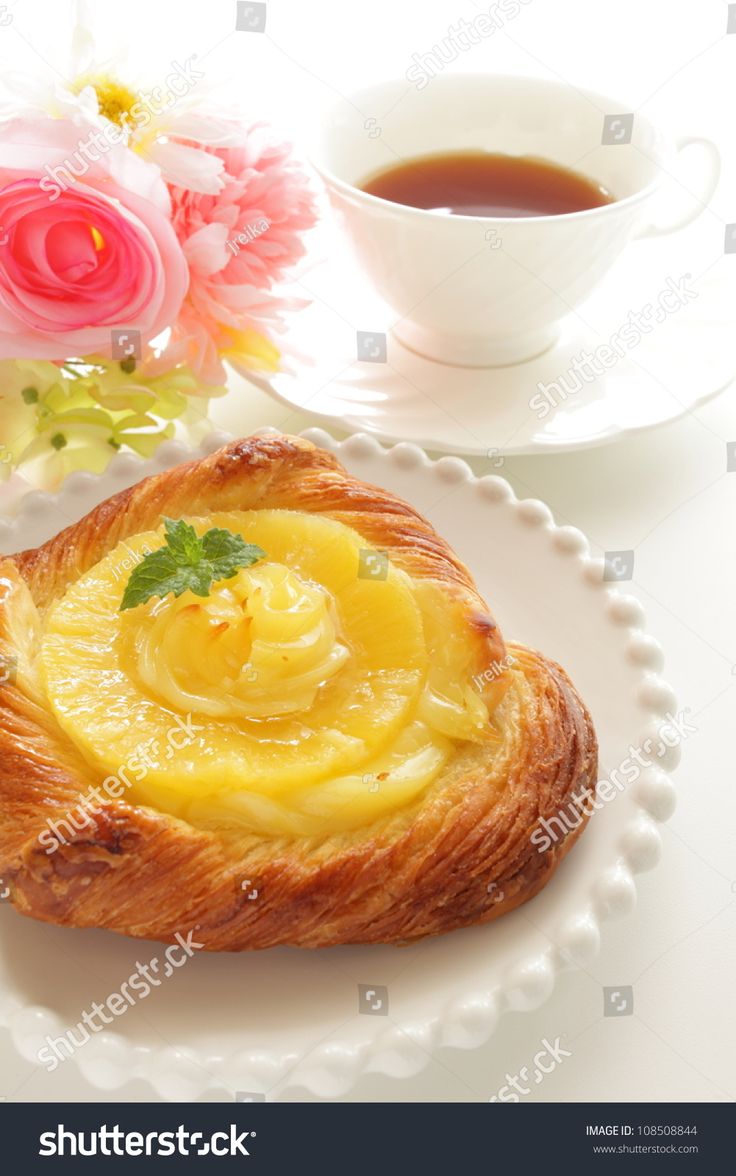 a pastry on a white plate next to a cup of tea and pink flower bouquet