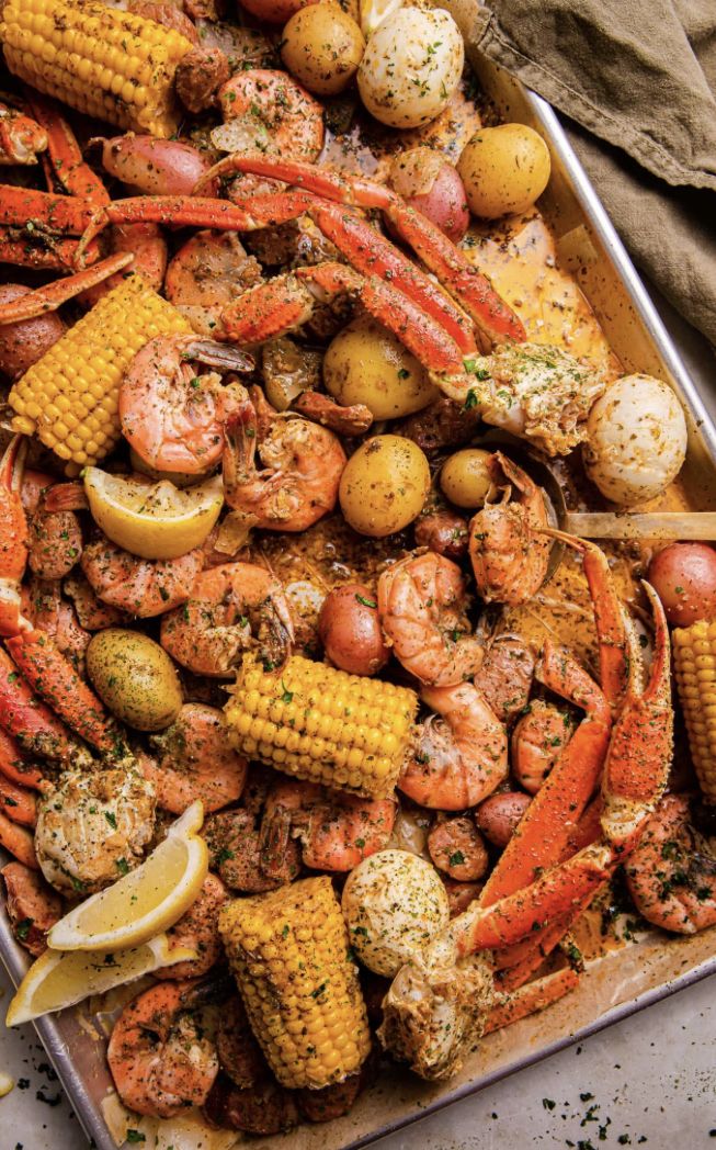 lobster, corn on the cob and potatoes with lemon wedges in a pan