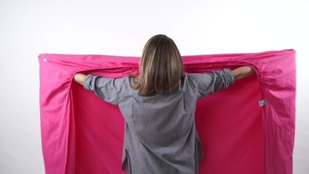 a woman is standing in front of a pink sheet with her hands on the back of her head