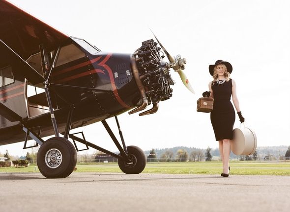 a woman in a black dress and hat standing next to an airplane