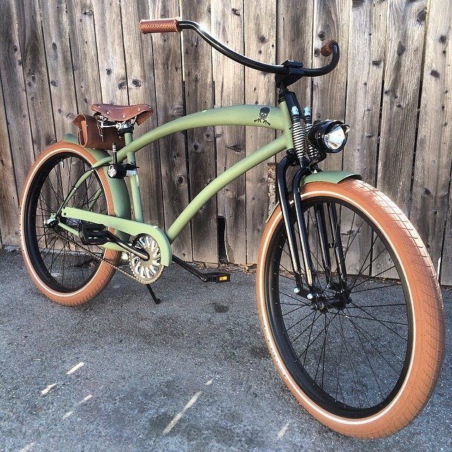 an old fashioned green bicycle parked in front of a wooden fence with brown leather seat