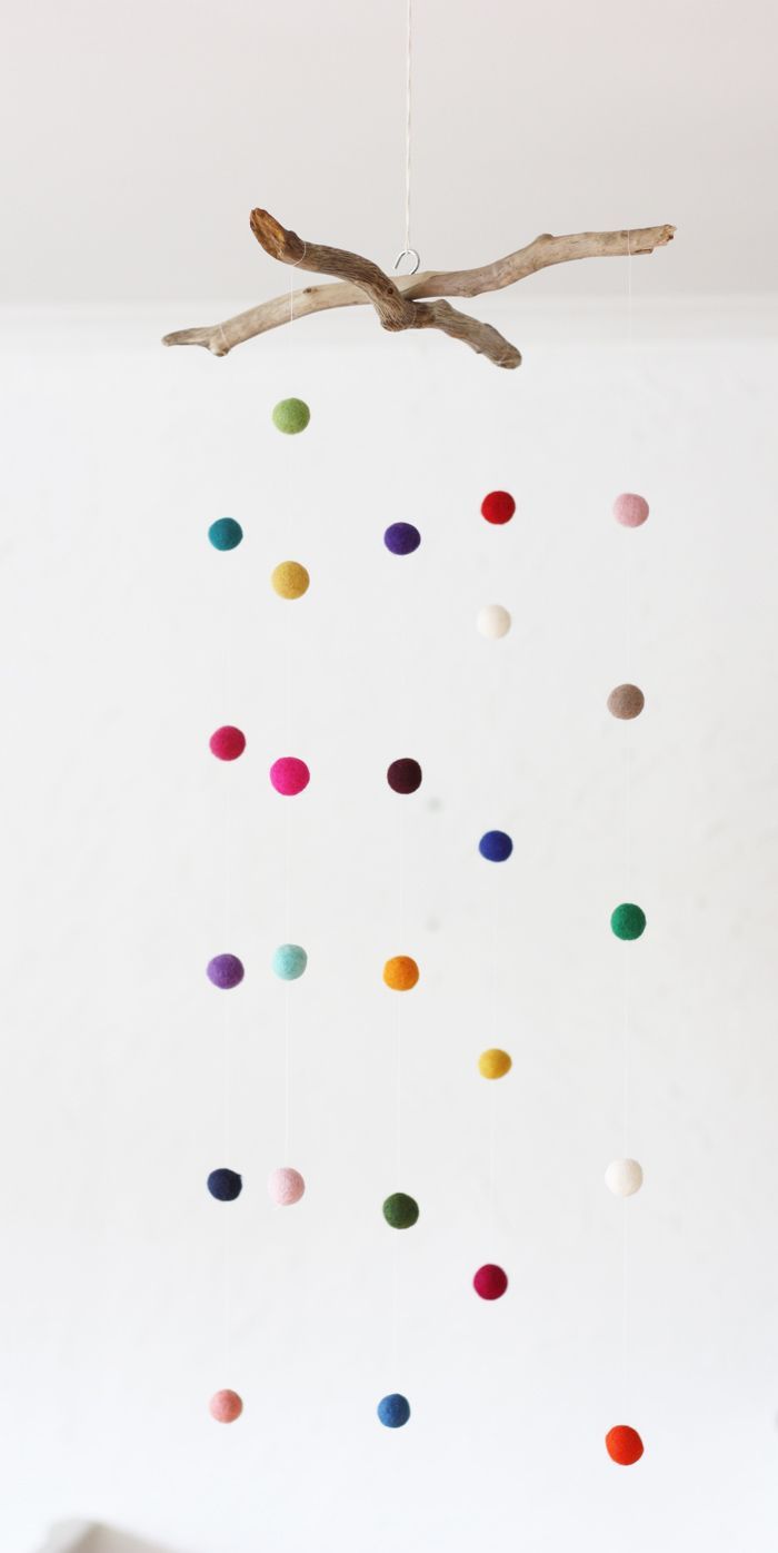 a mobile made out of different colored balls hanging from a tree branch in a white room