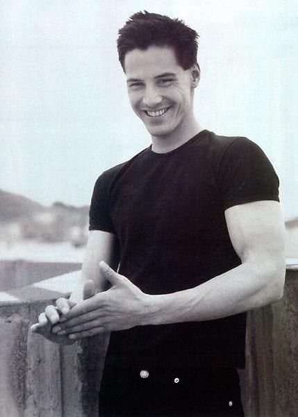 a man standing next to a wooden fence with his hands in the air and smiling