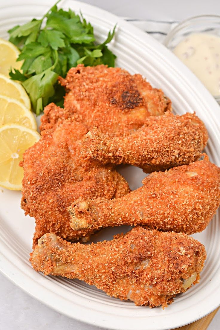 some fried food on a white plate with lemon wedges and greens next to it