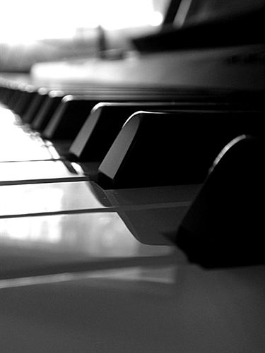 black and white photograph of piano keys with sunlight coming through the window behind them,