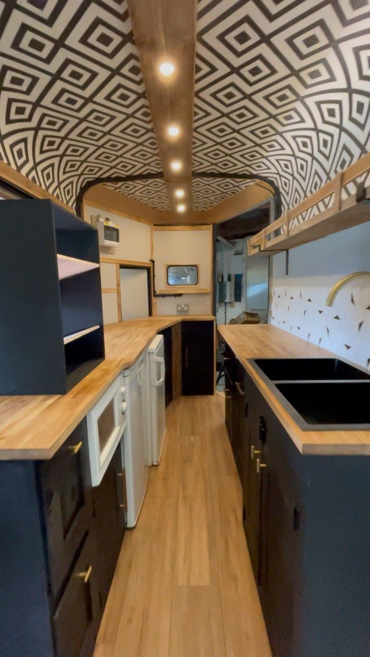 the interior of an rv with wood flooring and black cabinets, white appliances and patterned ceiling