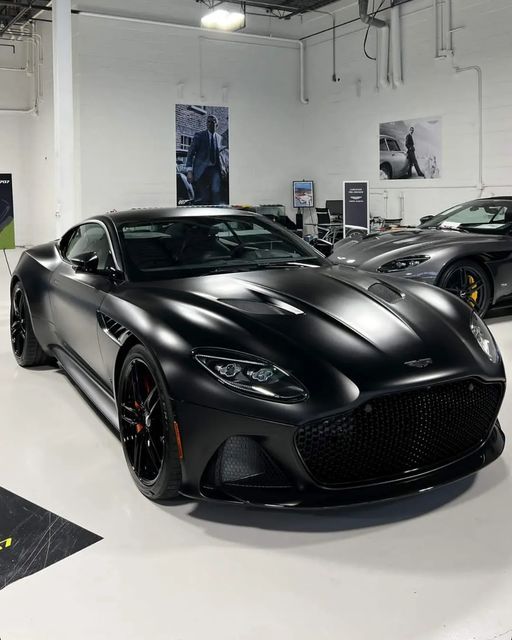 two black sports cars in a showroom with other vehicles on the wall behind them