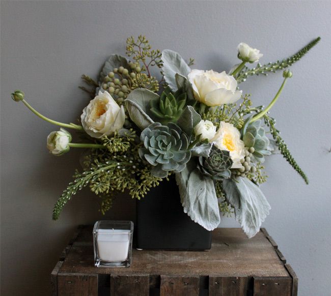 a vase filled with white flowers on top of a wooden table next to a candle