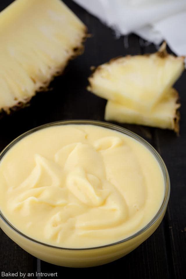 a glass bowl filled with cream next to sliced pineapples