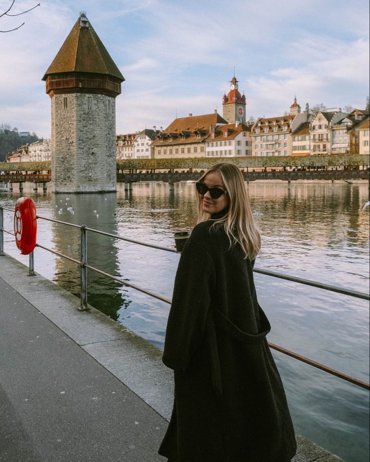 a woman standing next to a river with buildings in the background