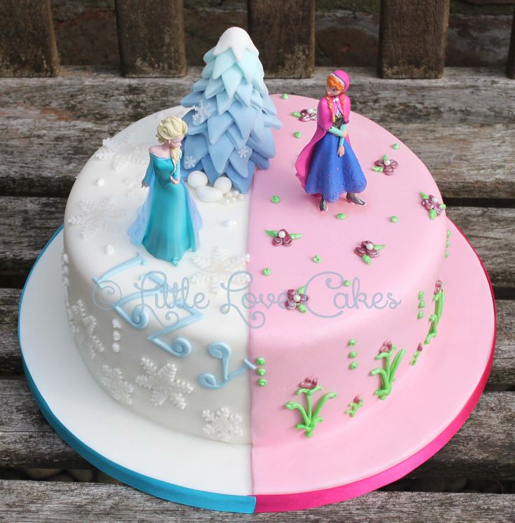 two cakes decorated with frozen princess and snowflakes on top of each other, sitting on a wooden bench