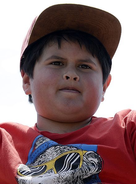 a young boy wearing a red shirt and brown hat with his hand up in the air