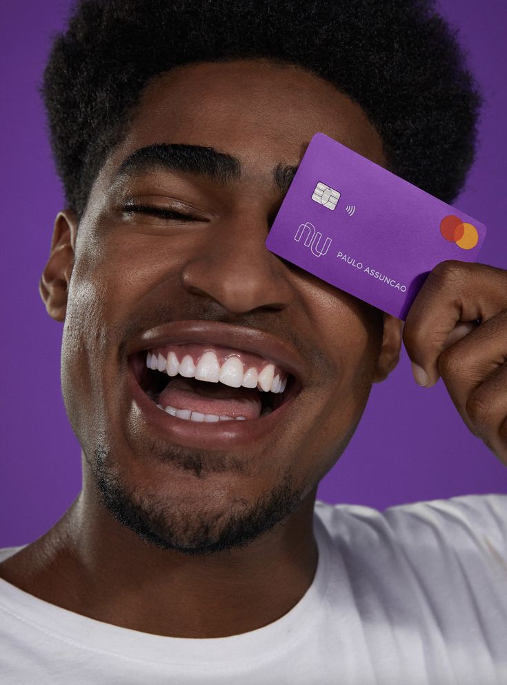 a man holding up a purple credit card to his eye and smiling at the camera