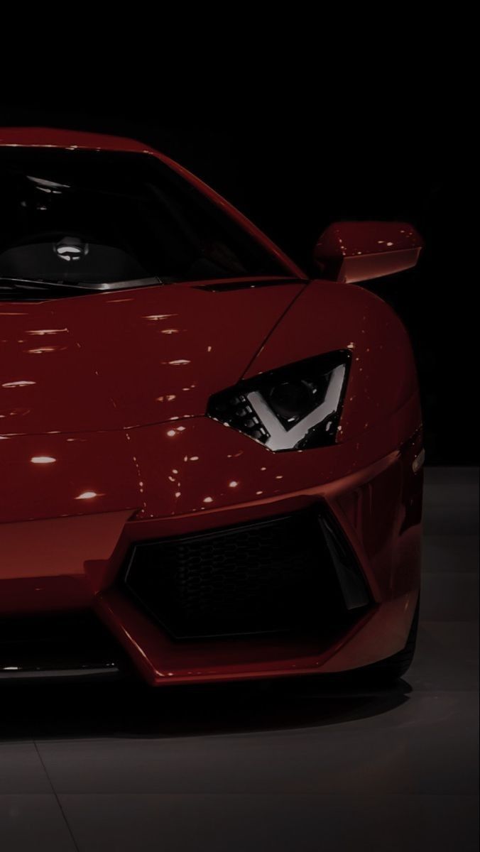 the front end of a red sports car in a dimly lit area with its lights on