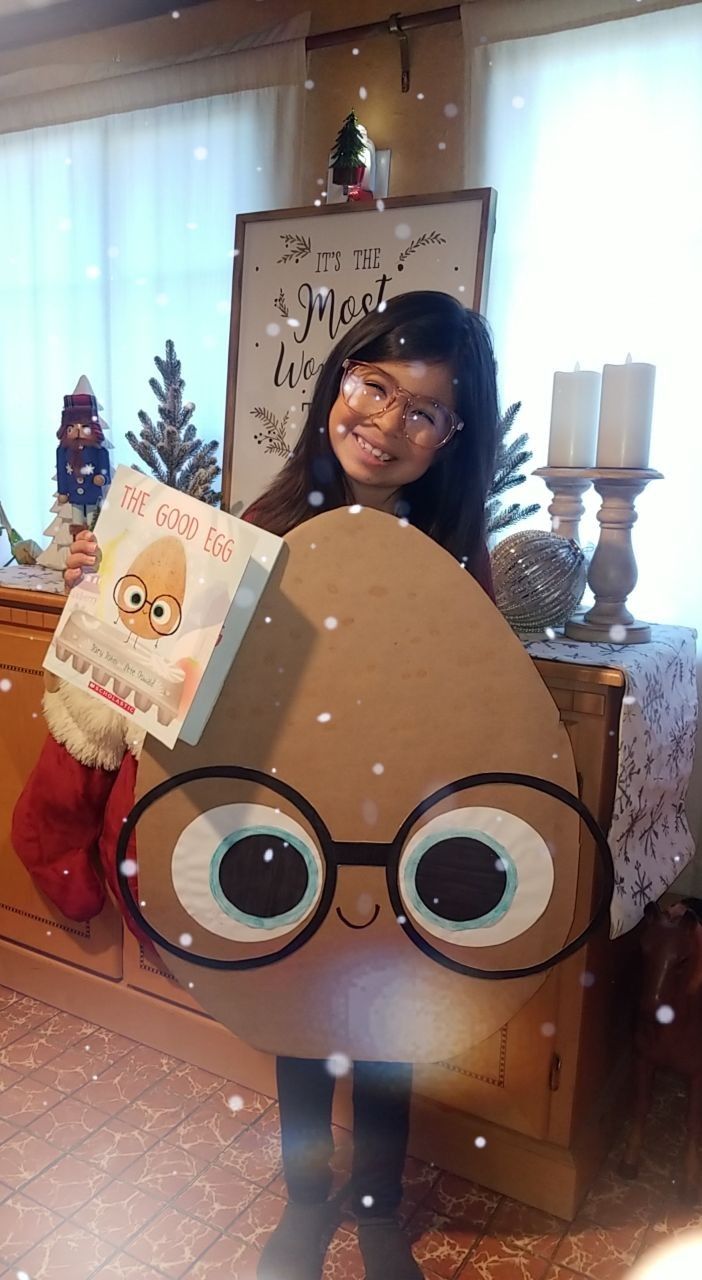 a woman holding up a cardboard cut out of a cartoon character with glasses and a book in front of her face