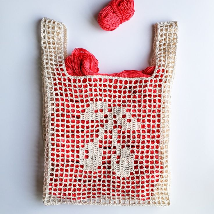 a red and white bag with two balls of yarn in it on a white surface