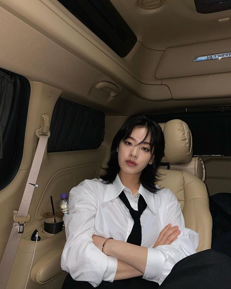 a woman sitting in the back seat of a car wearing a black tie and white shirt