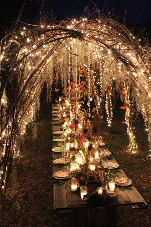 a long table covered in candles and lights under an arbor with branches that have been lit up