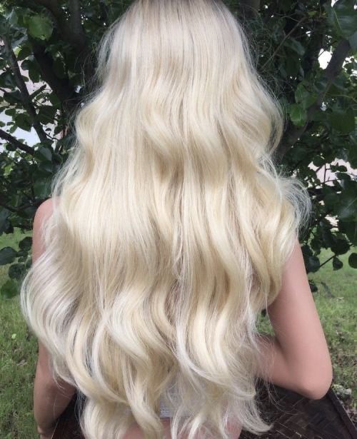 the back of a woman's head with long, blonde hair sitting in front of a tree