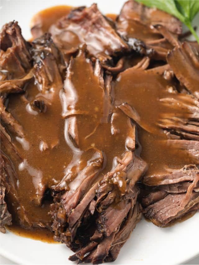 a white plate topped with roast beef covered in gravy and garnished with green leaves