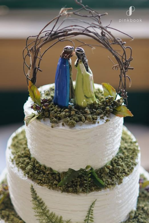 a three tiered cake decorated with figurines and greenery on the top