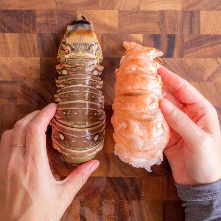 two hands holding an object on top of a wooden table next to another person's hand