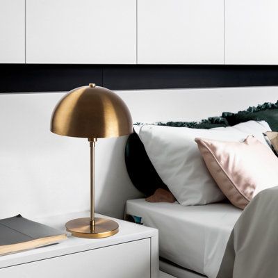 a bed with white sheets, pillows and a gold lamp on the nightstand next to it