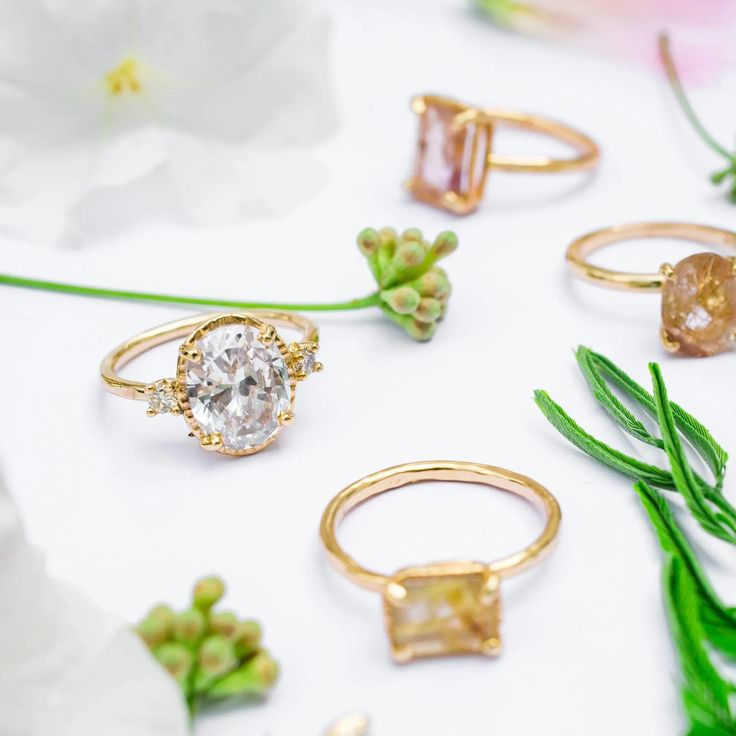 several different types of rings sitting next to each other on a white surface with flowers in the background