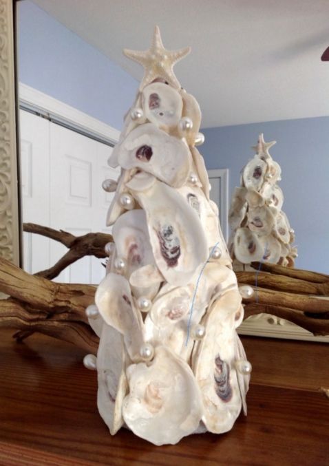 a white christmas tree made out of seashells on a wooden table in front of a mirror