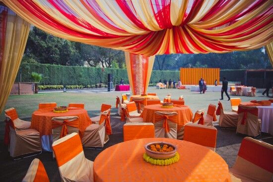 an outdoor event with orange and white linens on the ceiling, tables set up for dinner