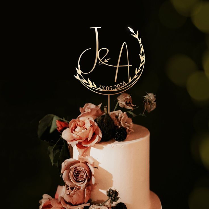 a wedding cake with pink flowers and a monogrammed initials on top is shown