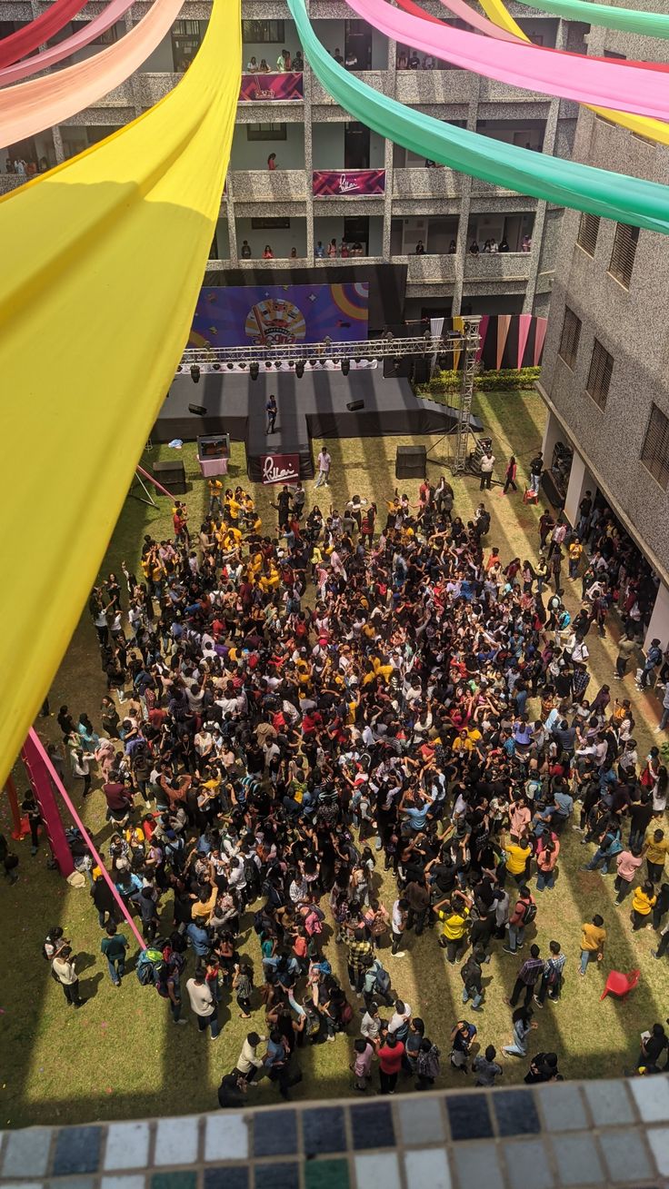 a large group of people standing around each other in front of a building with colorful ribbons hanging from the ceiling