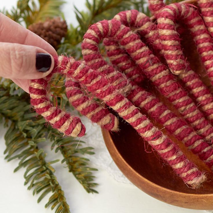 someone is holding up some red and white knitted items in front of pine branches