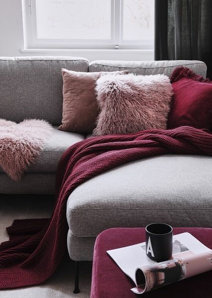 a couch with pillows and blankets on it in front of a window next to a coffee table