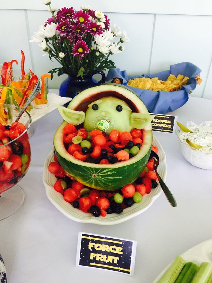 a watermelon carved to look like a baby yoda in a fruit bowl