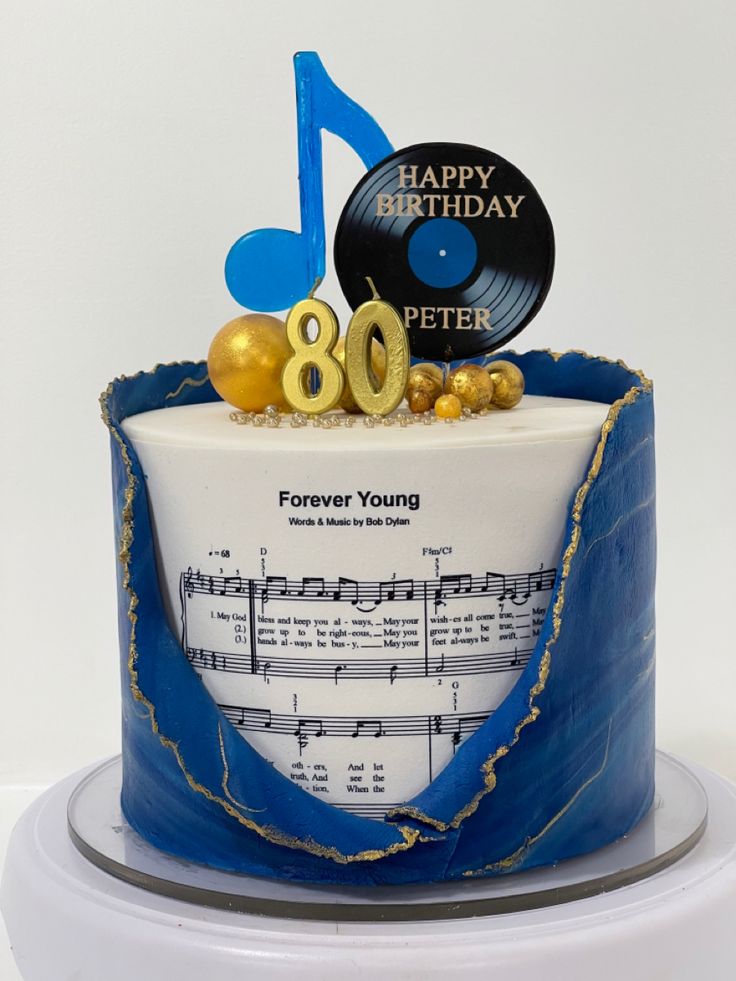 a birthday cake decorated with music notes and gold foil decorations is on a white pedestal